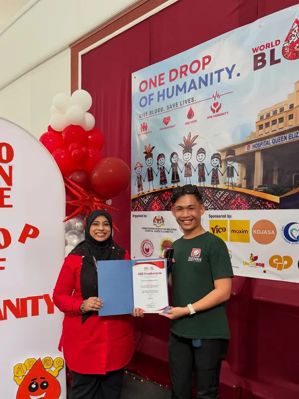 Receiving a certificate of appreciation under the One Drop of Humanity banner at the World Blood Donor Day campaign, Hospital Queen Elizabeth II